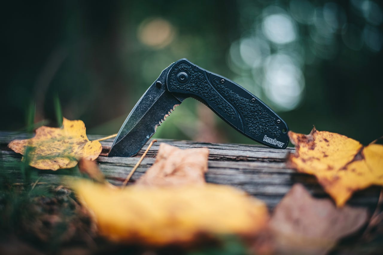 Folding knife on a wooden log surrounded by autumn leaves.
