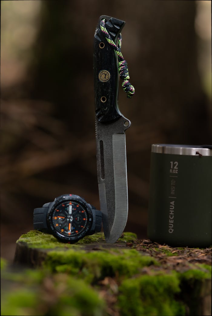 service-03 A knife, wristwatch, and metal cup on a moss-covered stump in a forest setting.